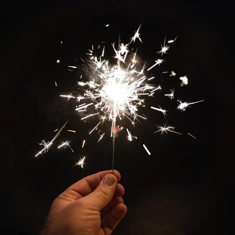 Hand holding a lit sparkler against a dark background